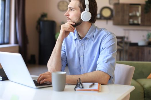 Happy young man in earphones working on laptop from home during self isolation