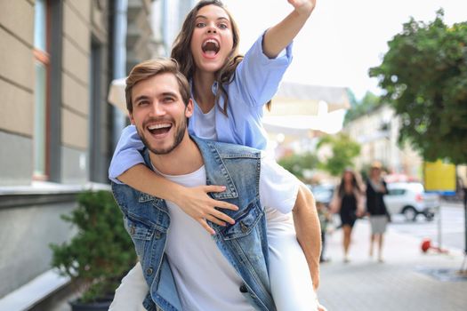 Handsome young man carrying young attractive woman on shoulders while spending time together outdoors