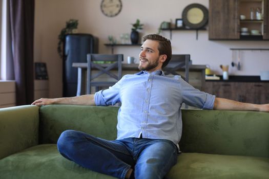 Handsome young business man is looking relaxed while sitting on the couch at home