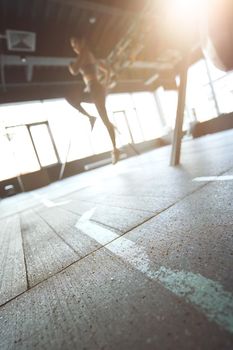 Sport training concept. Vertical shot of athletic woman in sportswear working out at industrial gym, focus on the floor. Wellness and healthy lifestyle