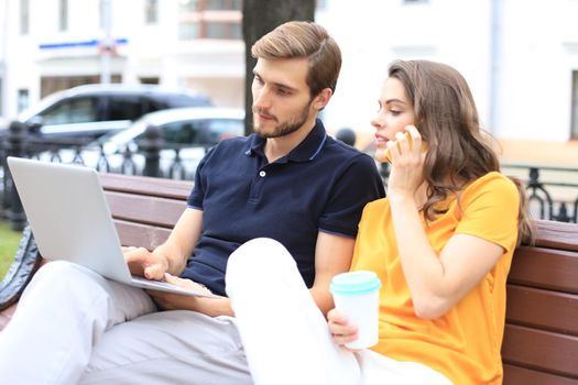 Attrative young couple using laptop computer while sitting on a bench outdoors