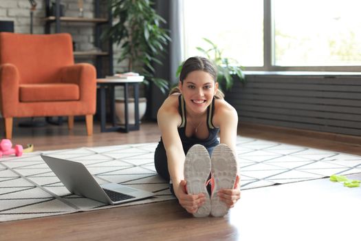 Fitness beautiful slim woman doing fitness stretching exercises at home in the living room. Stay at home activities. Sport, healthy lifestyle