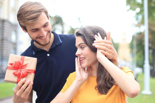 Image of charming excited couple in summer clothes smiling and holding present box outdoor