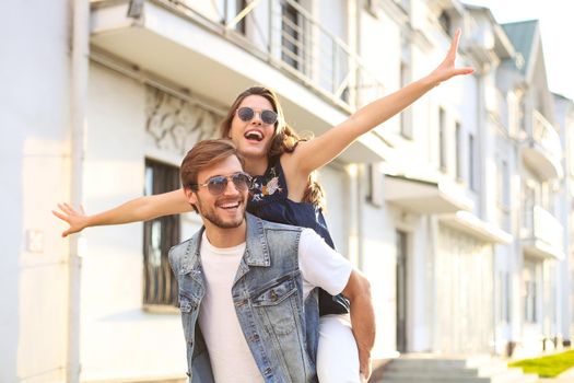 Handsome young man carrying young attractive woman on shoulders while spending time together outdoors