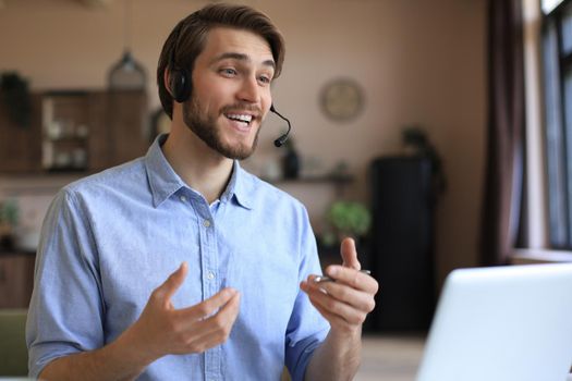 Cheerful young support phone male operator in headset, at workplace while using laptop, help service and client consulting call center concept.