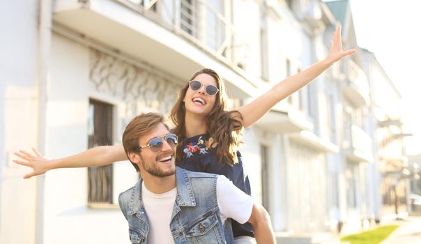 Handsome young man carrying young attractive woman on shoulders while spending time together outdoors