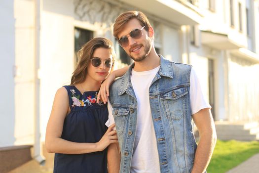 Image of lovely happy couple in summer clothes smiling and holding hands together while walking through city street