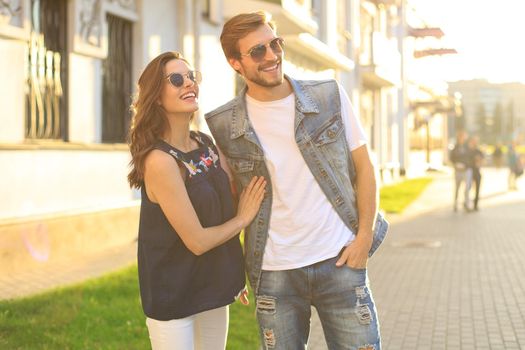 Image of lovely happy couple in summer clothes smiling and holding hands together while walking through city street