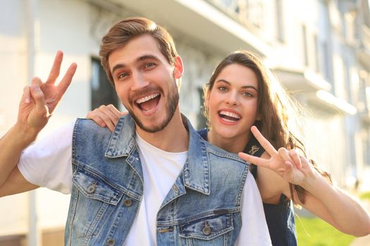 Image of a happy smiling cheerful young couple outdoors take a selfie by camera showing peace