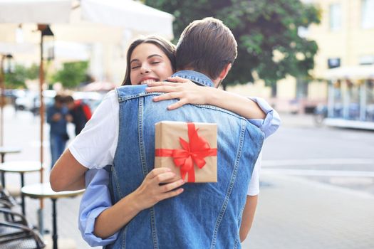 Image of attractive woman with present box giving hug to her man