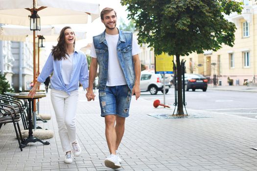 Image of lovely happy couple in summer clothes smiling and holding hands together while walking through city street