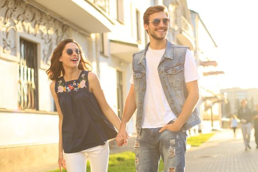Image of lovely happy couple in summer clothes smiling and holding hands together while walking through city street