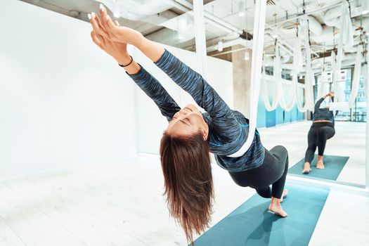 Relaxation. Young caucasian fitness woman in sportswear practicing fly yoga in front of the mirror wall in beautiful bright studio. Sport, wellness and healthy lifestyle, aerial yoga concept