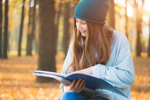 Nice student reading textbook on natural autumn background