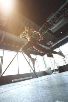 Bottom view of athletic woman in sportswear jumping or running while working out at industrial gym, vertical shot. Sport, training, wellness and healthy lifestyle