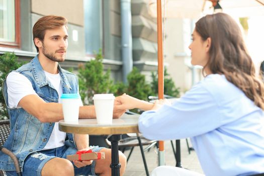 Smiling young girl having a date with her boyfriend at the coffee shop, man holding present box