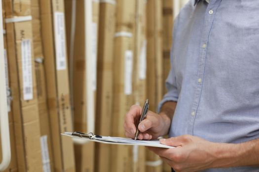 Young man shopping or working in a hardware warehouse standing checking supplies on his tablet