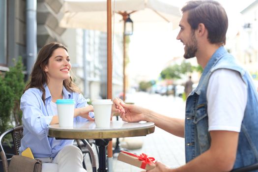 Smiling young girl having a date with her boyfriend at the coffee shop, man holding present box