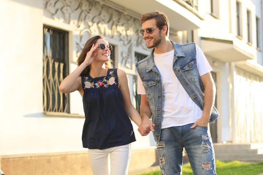 Image of lovely happy couple in summer clothes smiling and holding hands together while walking through city street