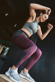 Best calorie burning Exercises. Bottom view of a strong athletic woman in sportswear doing box jump while working out at industrial gym, vertical shot. Sport, wellness and healthy lifestyle