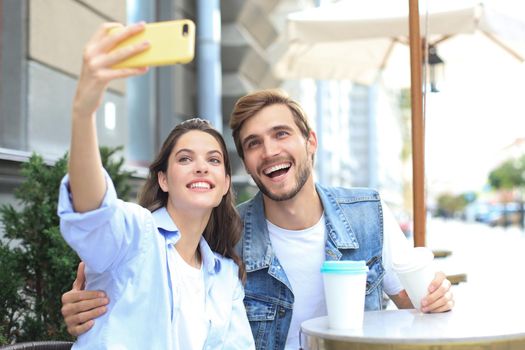 Beautiful young loving couple bonding to each other in cafe while woman making selfie by smart phone