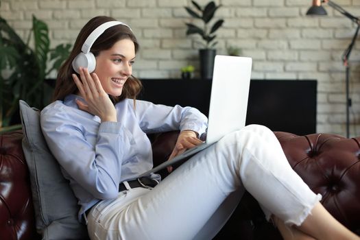 Smiling young woman with headphones and laptop on the sofa
