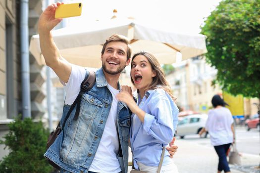 Beautiful lovely young couple walking at the city streets, hugging while taking a selfie