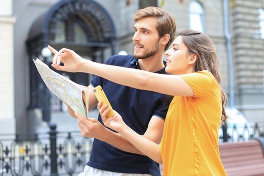 Beautiful young couple holding a map and smiling while standing outdoors