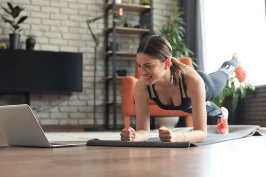 Beautiful fitness woman doing a plank exercise watching online tutorials on laptop, training in living room. Healthy lifestyle. Girl goes in for sports at home.