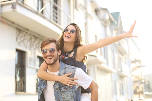 Handsome young man carrying young attractive woman on shoulders while spending time together outdoors