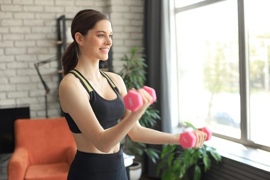 Young beautiful sports girl in leggings and a top does exercises with dumbbells. Healthy lifestyle. A woman goes in for sports at home