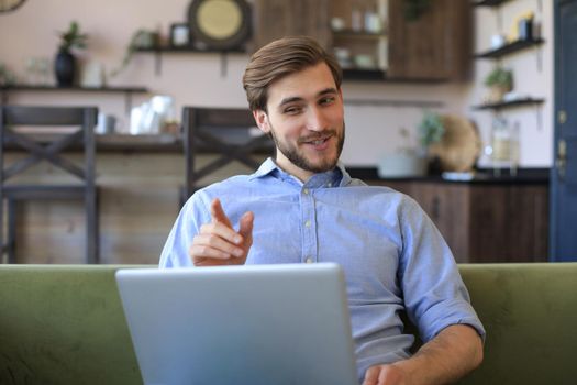 Smiling businessman greeting colleagues in video conference and negotiating distantly from home