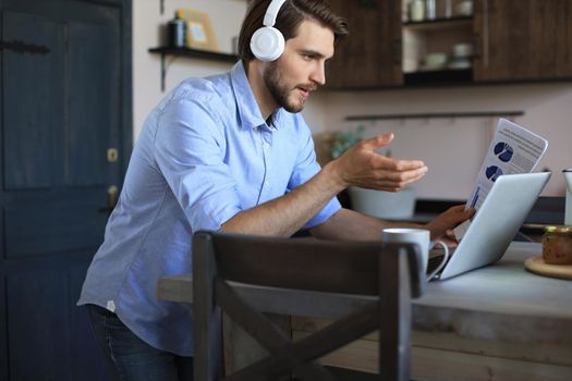 Smiling businessman greeting colleagues in video conference and negotiating distantly from home