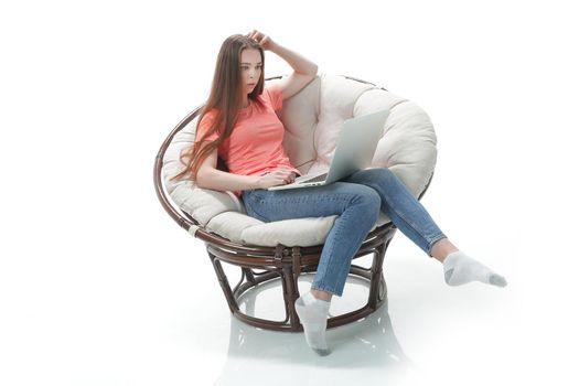 young woman works on a laptop sitting in a comfortable chair.