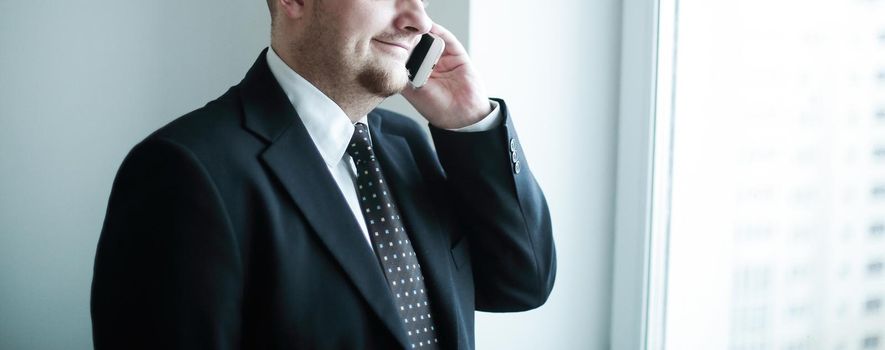 handsome pensive businessman using smartphoone and looking through window in the office.photo with copy space