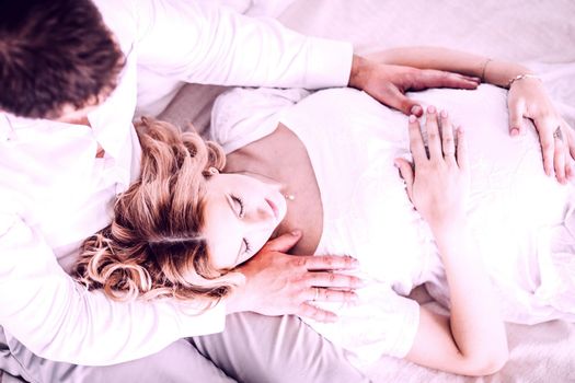 caring husband hugs his pregnant wife while sitting on the bed.