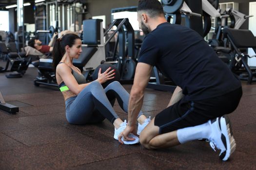 Trainer helping young woman to do abdominal exercises in gym