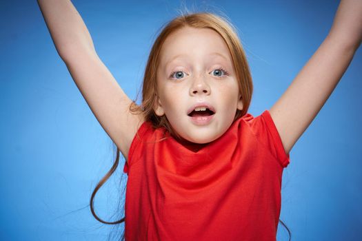 cute red-haired girl in red t-shirt emotions blue background. High quality photo