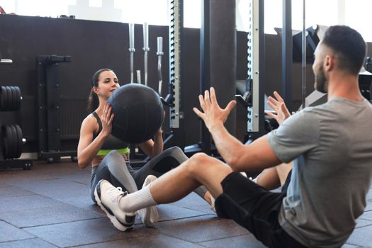 Beautiful young sports couple is working out with medicine ball in gym