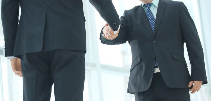 Closeup of handshake of two entrepreneurs wearing business suit, shot against bokeh background
