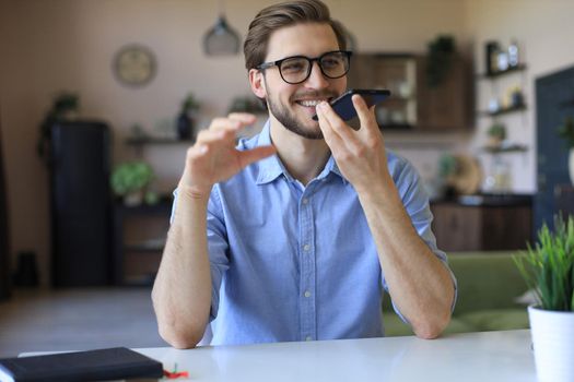 Confident business man in glasses holding smartphone near mouth for recording voice message or activating digital assistant
