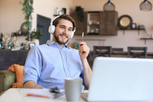 Happy young man in earphones working from home during self isolation