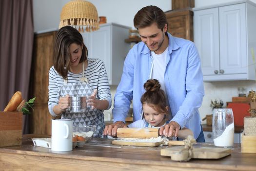 Cute little girl and her parents are having fun while cooking in kitchen at home together