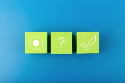 Target, question sign and checkmark on green toy cubes on dark blue background Concept of goal, success, reaching business and personal aims