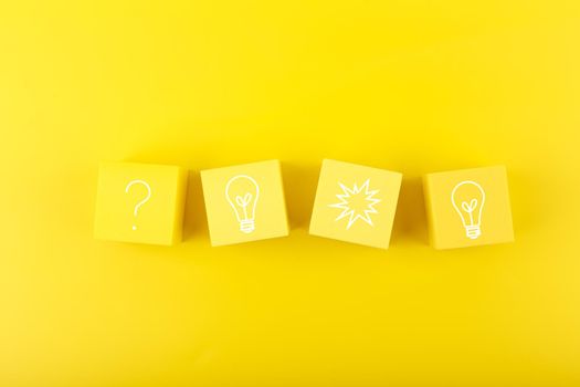 Concept of idea, creativity, start up or brainstorming. Light bulb and question signs drawn on toy cubes on yellow background