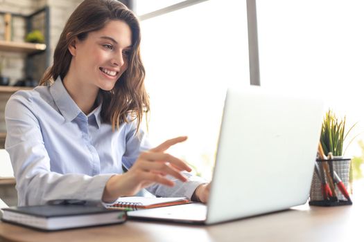 Smiling pretty woman sitting at table, looking at laptop screen. Happy entrepreneur reading message email with good news, chatting with clients online