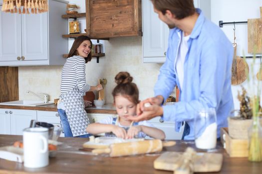 Cute little girl and her parents are having fun while cooking in kitchen at home together