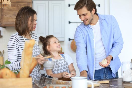 Cute little girl and her parents are having fun while cooking in kitchen at home together