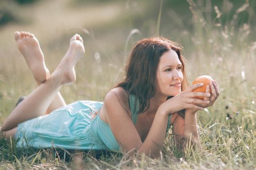 thoughtful young woman with orange lying on the lawn. photo with copy space