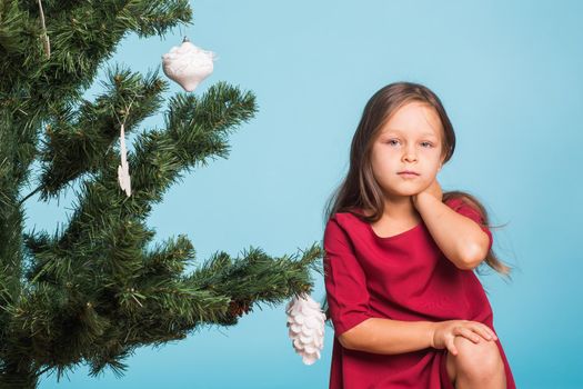 Little girl with christmas tree on blue background.